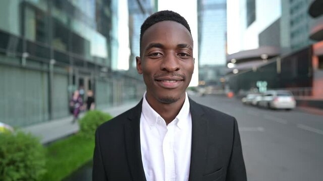 Portrait of a young black guy on the street against the background of a business center. Young man in shirt and jacket, office worker or businessman smiling