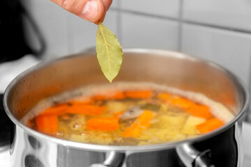 The chef cooks Finnish salmon soup. The cook puts a bay leaf in a saucepan. High quality photo