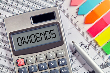 Office desktop with calculator displaying the word dividends. Financial share or revenue in business