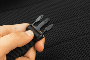 A semi-automatic fastener of the travel backpack on the man hand close-up, black belts nylon background