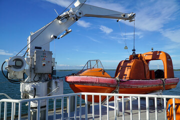 Orange lifeboat, rescue boat of ferry boat sailing on the sea with blue sky and coastline in the...