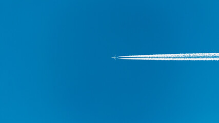 an airliner cuts the blue sky in half. traces of jet engines leave smooth stripes on the clear blue sky