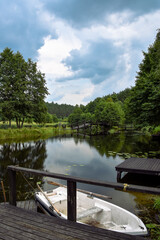 Small boat floating on a little lake, neat to wooden jetty, bridge and forest in the background