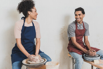 partial view of young african american couple looking at each other and modeling wet clay on wheels with hands in pottery