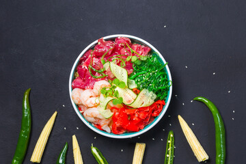 Poke with tuna and shrimp, and seaweed salad. Top view on a black background with mini corn and green pepper pods. Horizontal, with space