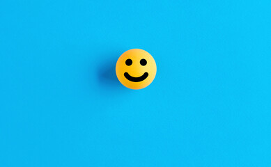 Smiling face emoticon or icon on a ball on blue background. Positive feedback