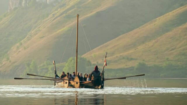 Vikings Sail on an Old Ship with a Lowered Sail on a Quiet River in the Fog. Concept on the theme of the Vikings and the early Middle Ages.