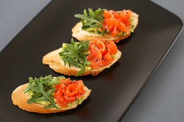 Tartlet from the buffet, on a black plate, red fish and arugula, a delicious snack before the main course.