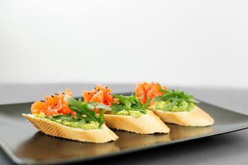 Tartlet from the buffet, on a black plate, red fish and arugula, a delicious snack before the main course.