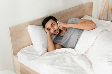 Young man talking on cellphone while lying on bed