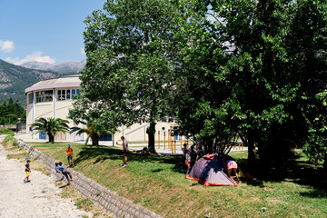 Children and adults are engaged in rope climbing on the slope against the backdrop of greenery, trees and tent