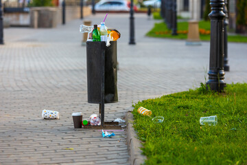 overflowing trash can on the sidewalk pavement at summer daylight