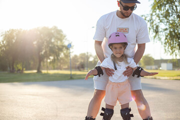 Father teaching his daughter to skate on roller skates. Happy kid in helmet learning skating....
