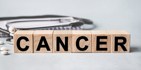 CANCER inscription on wooden cubes isolated on white background, medicine concept. Nearby on the table are a stethoscope and pills.