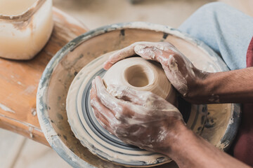 Fototapeta premium close up view of young african american man modeling wet clay on wheel with hands in pottery