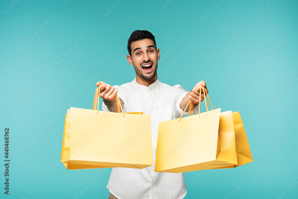 Wall mural excited arabian man holding shopping bags isolated on blue