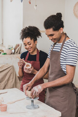 smiling young african american man and woman sculpting clay pot in pottery