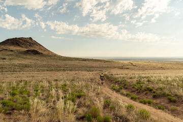 A lone cyclist on a dirt trail through a field of shrubs and brush at the foot of a small mountain, Petroglyph NM, New Mexico