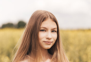 Portrait of a beautiful young girl with long hair against the background of rapeseed flowers. Youth and nature