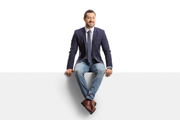 Full length portrait of a man in jeans and suit sitting on a blank panel - obrazy, fototapety, plakaty