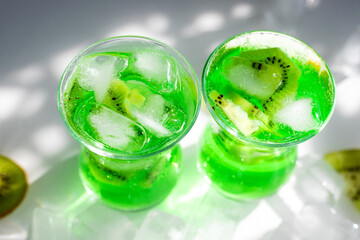 Green lemonade with ice and kiwi slices.Two glass glasses stand on the table and the sun's rays fall on them.