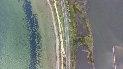 A highway that runs along a narrow spit between the sea and the estuary. Cars on the road. Aerial view.