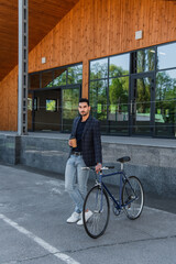 Muslim businessman with takeaway drink looking at camera near bike outdoors