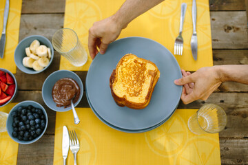 Hands placing a plate of french toast on a picnic table