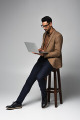 Arabian businessman using laptop on chair on grey background