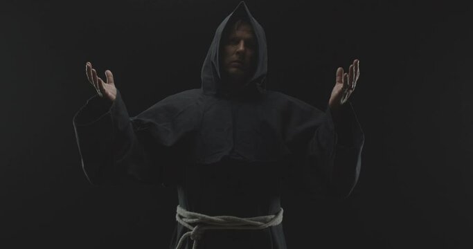 Monk Hold His Hands up as if Praying in a Dark Background