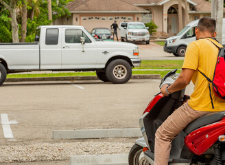 Man starting up a motor scooter with cars and a house in the background