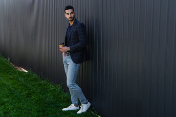 Young muslim businessman holding coffee to go near fence outdoors