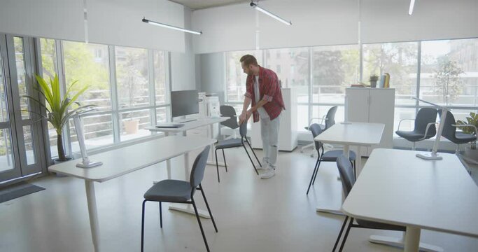 Young man putting chair down and working alone in empty office