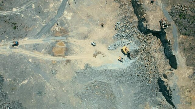 Arial view of the sand making plant in open-pit mining. Drone flies over excavators and tractor loading crushed stone and rock into dump truck. 4k stock footage.
