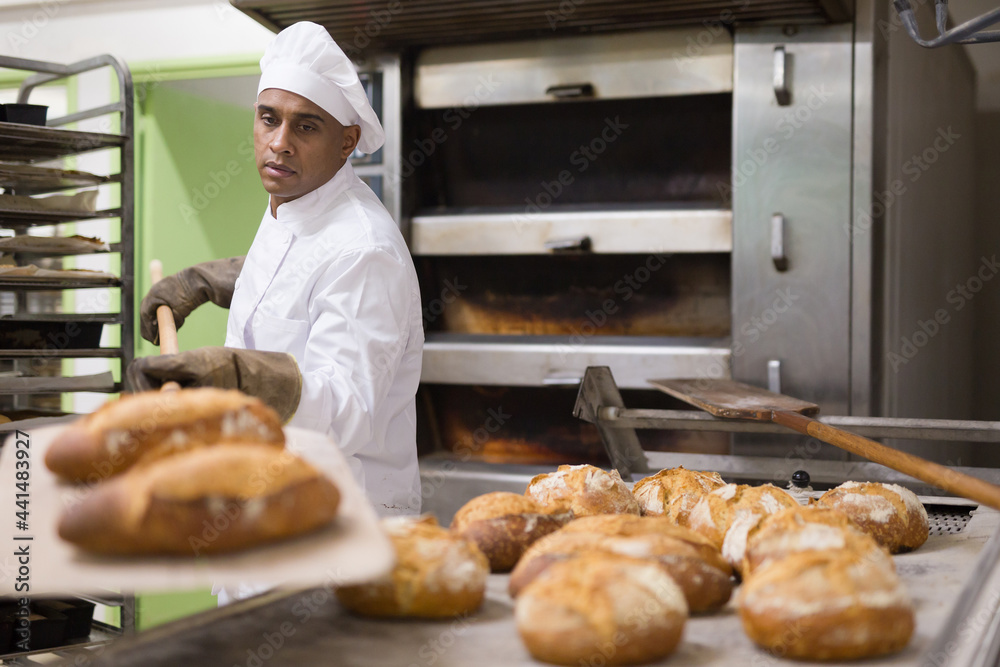 Wall mural male baker pulls hot bread out of the oven at the bakery