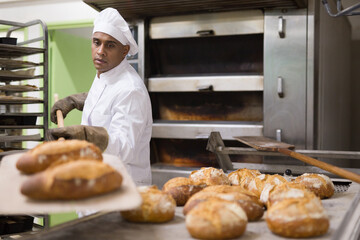 Male baker pulls hot bread out of the oven at the bakery