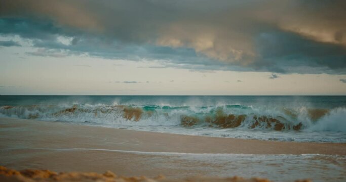 Ocean wave crashing on the beach at sunset in slow motion