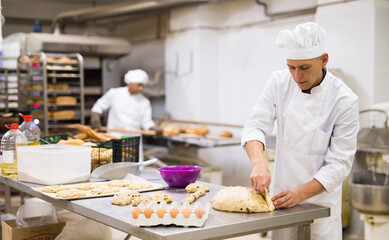 male baker in white uniform rolling out dough in kitchen