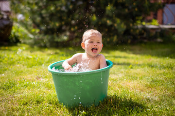 Baby girl flop in a green basin with water on home backyard in summer time - obrazy, fototapety, plakaty