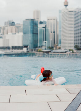 A little toddler girl swimming on a rooftop featuring the Sydney skyline in the background