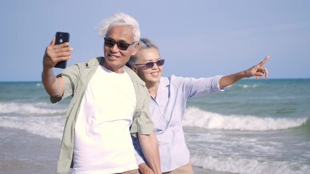Happy Asian senior man and woman couple smile taking selfie photo with smartphone on the beach, Romantic elderly enjoy Travel summer vacation, plan life insurance at retirement couple concept