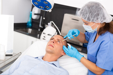 Young adult man patient of cosmetologist receiving hyaluronic acid injections