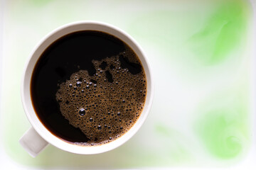 Top view of black coffee mug with bubbles on top, placed on the blurry floor looks like marble mixture of white and light green. Copy space.