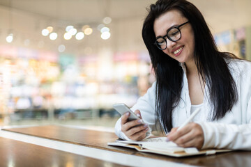 Happy Asian young woman sitting at cafe with coffee cup taking notes enjoying break