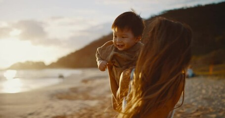 Attractive young mother playing with her baby son at the beach at sunset, family lifestyle moments