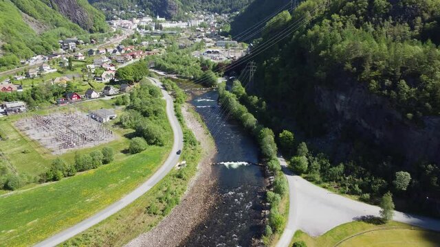 Dale salmon river with Dalekvam town-centre and BKK hydroelectric powerplant - High voltage power cables crossing in front of camera - River coming straight from powerplant - Aerial Norway