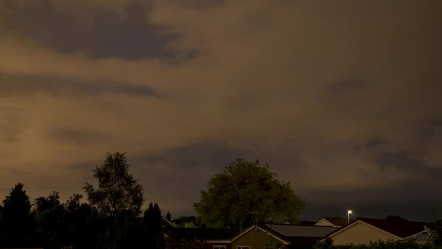Sunrise Time-lapse of fast moving clouds and stars on windy day above suburban rooftops and tree tops in the UK.