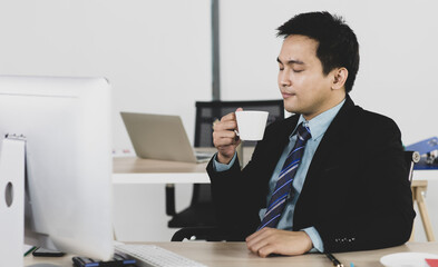 Naklejka premium Portrait focus to adult asian businessman are office people very smart and handsome hold coffee cup anก feeling comfortable smile on face. On desk have computer, calculator and tablet