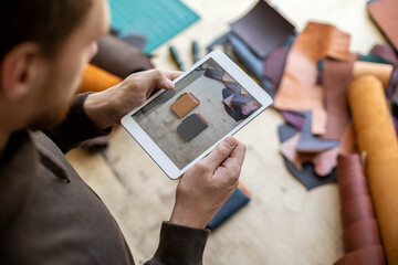 Top view male tanner use tablet at leather workshop. Craftsman creating online advertising promotion