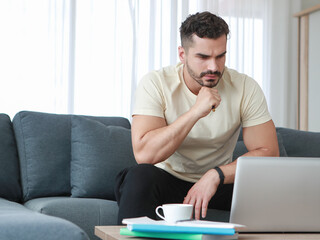 Fototapeta premium Thoughtful, serious Caucasian businessman working on laptop at home. Solving work problems and finding business inspiration concept.